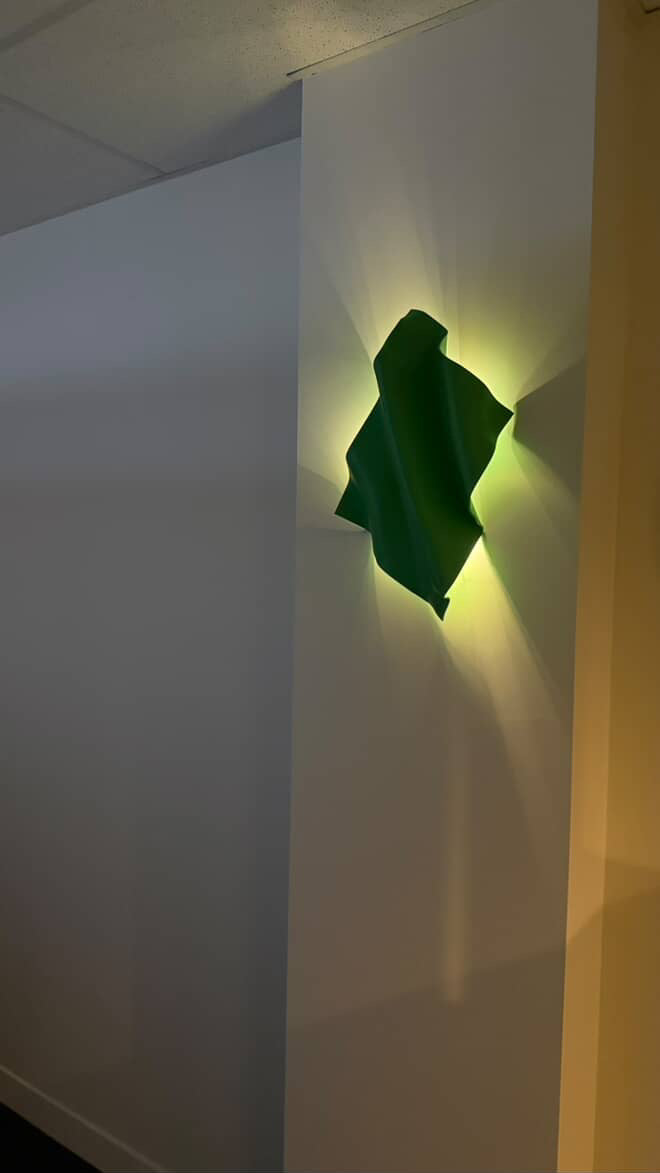 Green cloth draped over a white wall with a light source casting a shadow.