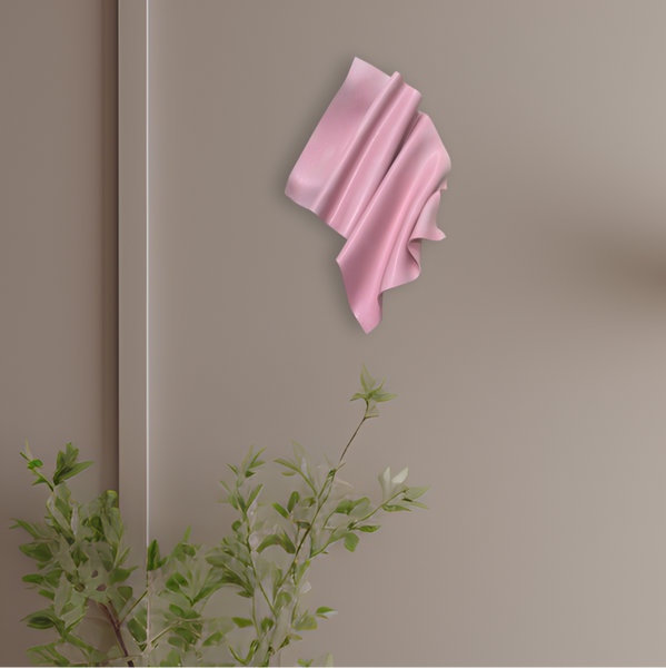 Pink decorative wall art on a beige wall with a plant in the foreground